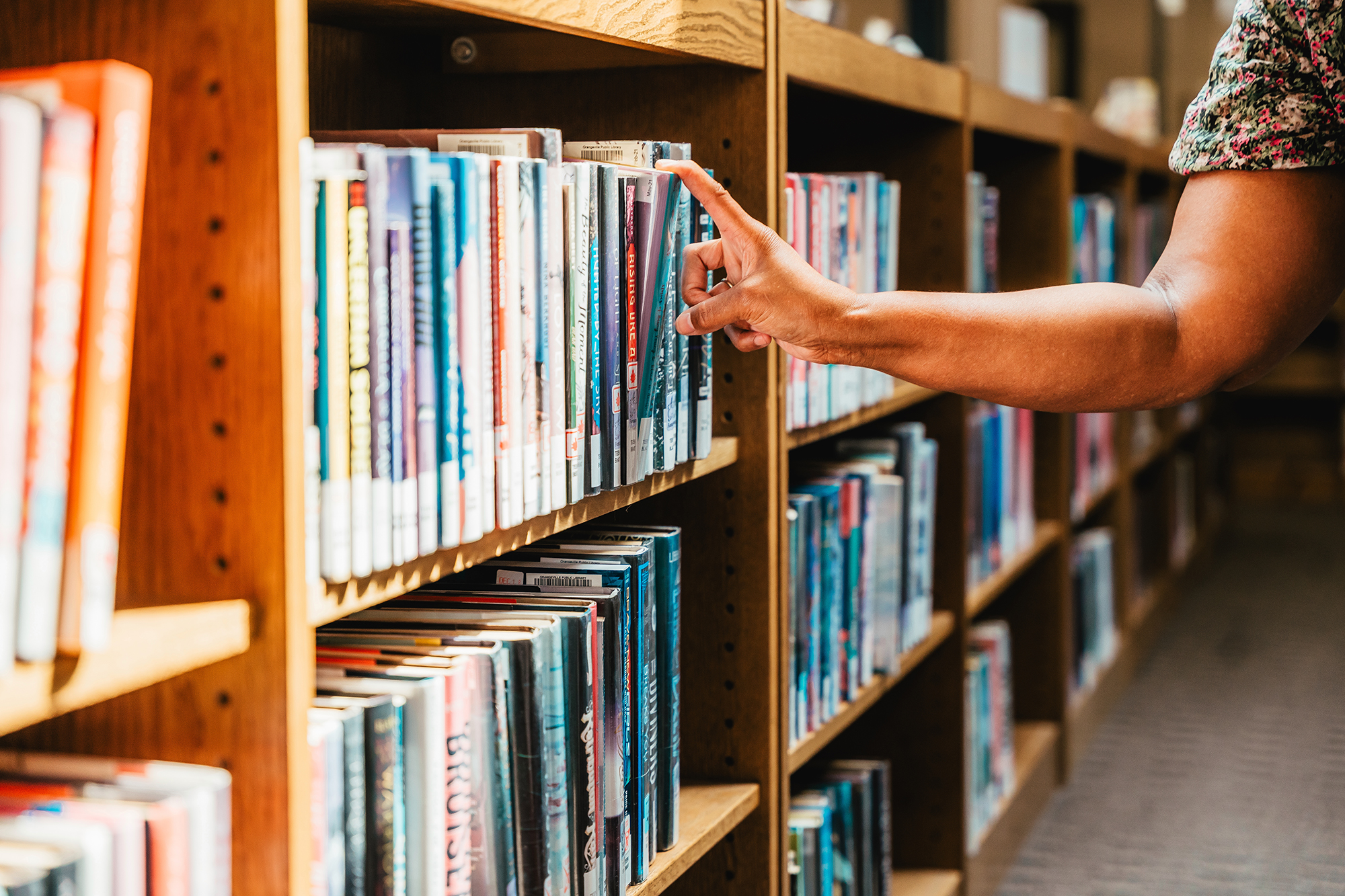 A hand reaches out to a book on a packed bookshelf in a library.